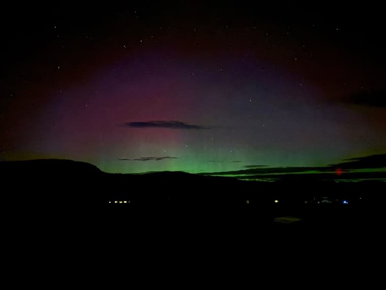Green and red northern lights over the hills